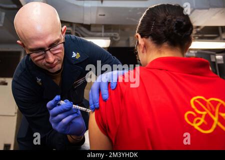 Philippinen-Meer. 7.. Dezember 2022. Hospital Corpsman 1. Klasse Alexander Roth, aus Dover, Tennessee, verabreicht den COVID-19-Impfstoff-Booster an die Flugbesatzung Survival Equipmentman Airman Kiana Briley, aus Savannah, Tennessee, auf der Achtermesse Decemberks an Bord der USA USS Ronald Reagan (CVN 76), der einzige Flugzeugträger der Navy in der Philippinischen See, Dezember. 7. Ronald Reagan, das Flaggschiff der Carrier Strike Group 5, ist eine kampfbereite Truppe, die die USA schützt und verteidigt und Allianzen, Partnerschaften und kollektive maritime Interessen in der Region Indo-Pazifik unterstützt. Stockfoto