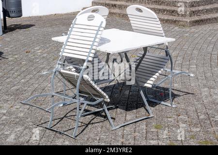 Ein Set altmodischer weißer Stühle und ein Tisch im Freien unter Sonnenlicht Stockfoto