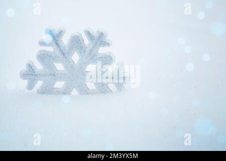 Eine Schneeflocke im Schnee. Weihnachtlicher Hintergrund mit dekorativer Schneeflocke auf Schnee. Weihnachtsdekoration. Winterferienkonzept Stockfoto