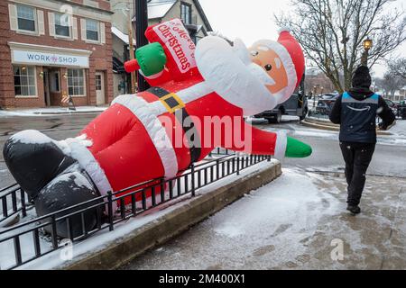 Chicago, USA. 16. Dezember 2022 Ein Mitarbeiter von Amazon Prime übergibt eine aufgeblasene Weihnachtsmann-Dekoration vor einem Geschäft in den Vororten von Chicago. Stockfoto