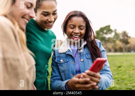 Drei multiethnische weibliche Freunde, die ihr Handy draußen halten Stockfoto