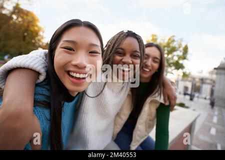 Eine Gruppe von drei fröhlichen Freundinnen, die in die Kamera schauen und sich umarmen Happy Girls draußen Stockfoto