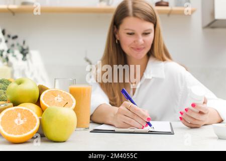 Ein fröhlicher Ernährungsberater schreibt einen Plan für die Einnahme von biologisch aktiven Nahrungsergänzungsmitteln und Vitaminen Stockfoto