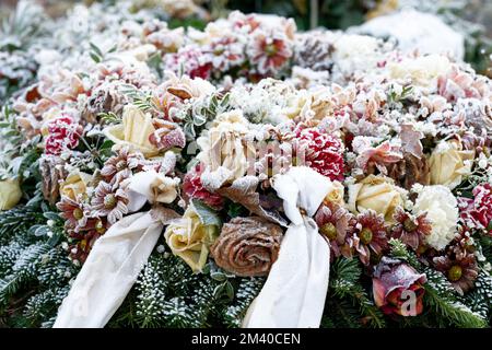 Bestattungskranz mit Schleife und farbenfrohen Pastellblumen auf einem Grab, bedeckt mit Eisfrost Stockfoto