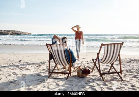 Ich genieße einen faulen Sommertag. Rückblick auf ein Paar mittleren Alters, das auf den Liegen am Strand sitzt. Stockfoto