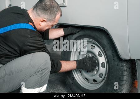 Der Mensch wechselt im Autodienst das Rad. Professioneller Automechaniker im Overall entfernt das Rad aus dem Lkw in der Garage. Authentischer Workflow... Stockfoto