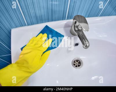 Handschuh aus gelbem Gummi mit Lappen, Wischtücher, weißes Waschbecken. Reinigung und Desinfektion mit Reinigungsmittel. Sauberes und glänzendes Waschbecken in der Toilette. Stockfoto