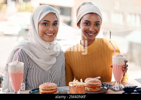 Wir waren super bereit, uns einzugraben. Gekürztes Porträt von zwei liebevollen jungen Freundinnen, die zusammen in einem Café essen, während sie in Hijab gekleidet sind. Stockfoto