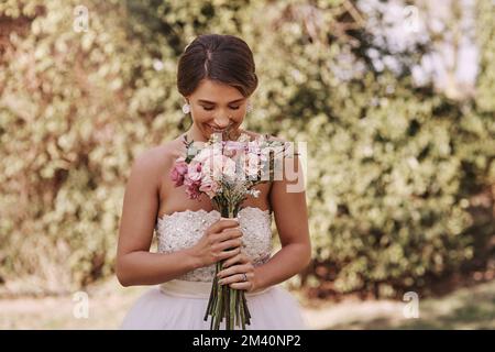 Sie riechen so unglaublich. Eine wunderschöne junge Braut, die am Hochzeitstag lächelt, während sie mit einem Blumenstrauß in der Hand steht. Stockfoto