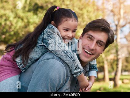 Steigen Sie in den Dad Express ein. Ein bezauberndes kleines Mädchen, das eine Huckepackfahrt mit ihrem Vater im Park genießt. Stockfoto