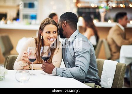 Ich denke, wir sollten ein Hotelzimmer buchen. Ein liebevoller junger Mann, der seinen Freundinnen ins Ohr flüstert, während er in einem Restaurant sitzt. Stockfoto