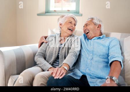 Lachen ist der Schlüssel zu einem glücklichen Leben. Ein Seniorenpaar, das sich zu Hause auf dem Sofa entspannt. Stockfoto