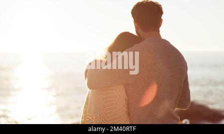 Der Sonnenuntergang ist so schön wie unsere Liebe füreinander. Rückblick auf ein junges Paar, das den Sonnenuntergang am Strand beobachtet. Stockfoto