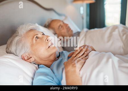 So viel zum Nachdenken. Eine nachdenkliche ältere Frau, die zu Hause im Bett neben ihrem schlafenden Ehemann liegt. Stockfoto