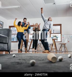 Heute geht es ihm definitiv besser. Gesamtbild eines Geschäftsmanns, der in seinem Büro Golf spielt, während seine Kollegen ihm im die Daumen drücken Stockfoto