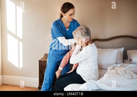 Verlässliche Hilfe von MORGENS bis ABENDS. Eine junge Krankenschwester hilft einer älteren Frau, sich in ihrem Schlafzimmer in einem Pflegeheim anzuziehen. Stockfoto