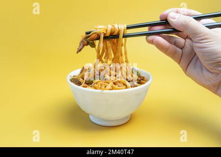 Udon Bratnudeln mit Hühnerfleisch und Sesam in der Schüssel auf gelbem Hintergrund in Nahaufnahme braten. Hellgelbe Hintergrundfarbe. Stockfoto