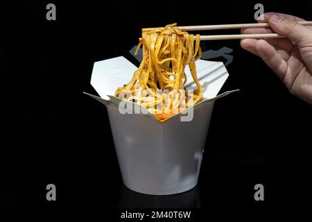 Schachtel mit Thai-Essen. Nudeln mit Huhn, Pilzen und Gemüse auf dunkelschwarzem Hintergrund Stockfoto