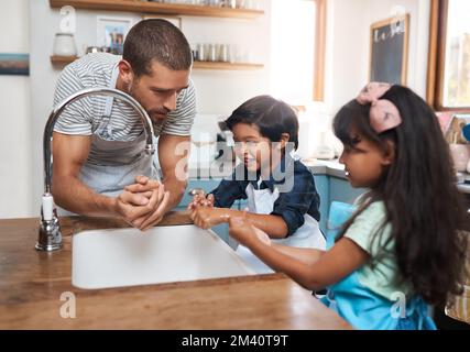 Lehre ihnen gesunde Gewohnheiten. Ein Mann und seine beiden Kinder waschen sich die Hände im Küchenbecken. Stockfoto