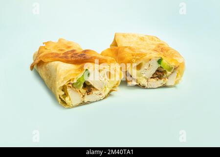Frisches Hühnerbrötchen mit frischem Gemüse, Salat, Käse und Zwiebeln auf hellblauem Hintergrund. Der Burrito ist in zwei Hälften geschnitten. Hellblaue Hintergrundfarbe Stockfoto