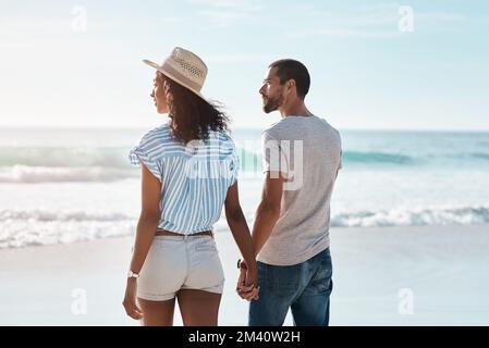 Die Sehenswürdigkeiten sind spektakulär. Rückblick auf ein junges Paar, das am Strand entlang spaziert. Stockfoto