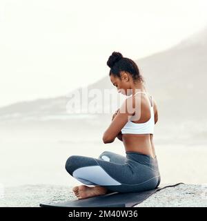 Körper mit Bewusstsein und Bewusstsein mit Seele vereinen. Eine sportliche junge Frau, die am Strand Yoga praktiziert. Stockfoto