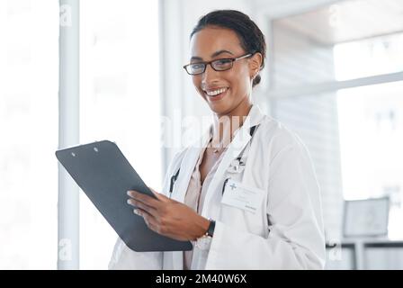 Verwaltung bedeutet Verantwortung für mich und die Patienten. Eine junge Ärztin, die eine Patienteninformation auf einem Klemmbrett aufzeichnet. Stockfoto