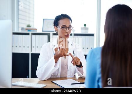 Wiederholen Sie dies zweimal täglich, bis der Kurs abgeschlossen ist. Eine junge Ärztin, die mit einer Patientin in ihrem Sprechzimmer spricht. Stockfoto