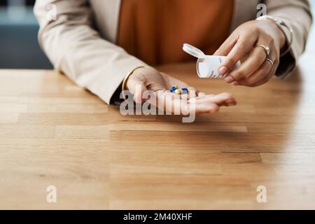 Wie viele soll ich nehmen? Eine nicht wiedererkennbare Geschäftsfrau, die Pillen aus einer Tablettenschachtel nimmt, während sie in ihrem Büro ist. Stockfoto