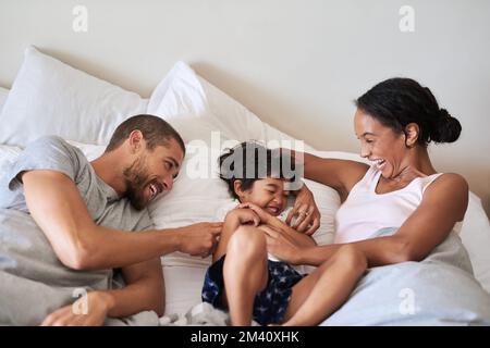 Es gibt nie einen langweiligen Moment, wenn er da ist. Eine wunderschöne dreiköpfige Familie, die zu Hause Zeit zusammen im Schlafzimmer verbringt. Stockfoto