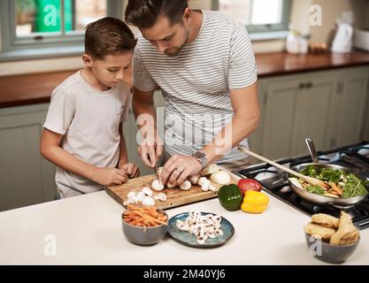 Pass nur auf, dass du dich nicht schneidest. Ein Junge, der seinem Vater beim Kochen hilft. Stockfoto