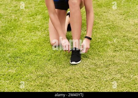 Schnürung und Mach dich fertig. Eine unbekannte junge Sportlerin, die beim Training auf der Rennstrecke ihre Schnürsenkel anzieht. Stockfoto