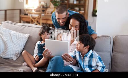 Wir sehen uns gerne lustige Videos online an. Eine vierköpfige Familie, die sich etwas auf einem digitalen Tablet ansieht. Stockfoto