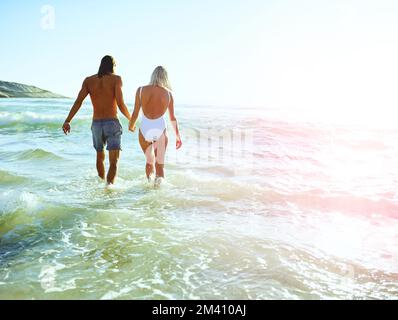 Verloren an ihrem glücklichen Ort. Rückblick auf ein junges Paar, das eine schöne Zeit am Strand genießt. Stockfoto