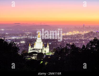 Der Oakland California Temple in den Hügeln von Oakland und die Skyline der Stadt unter farbenfrohem Himmel in der Abenddämmerung, Kalifornien Stockfoto