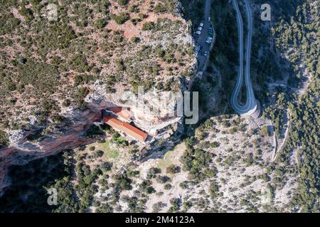 Gewundene Asphaltstraße, die die Berge überquert, führt zu orthodoxen Klostergebäuden im Felsen. Draufsicht Stockfoto