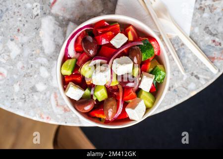 Griechischer Diät-Salat mit Feta, Tomaten, Grün auf hellem Hintergrund, Draufsicht. Gesundes Mittagessen. Lebensmittellieferungen auf Einwegteller aus Handwerkspapier. Umweltfreundlich Stockfoto