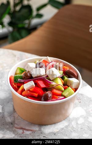 Griechischer Diät-Salat mit Feta, Tomaten, Grün auf grauem Steinhintergrund. Konzeptessen Für Partys. Fast Food. Gesundes Mittagessen. Lebensmittellieferung im Entsorgungsraum Stockfoto