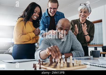 Wir haben ihm alle die Daumen geworfen. Ein erwachsener Geschäftsmann, der in seinem Büro Schach spielt, während seine Kollegen im Hintergrund zuschauen. Stockfoto