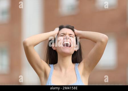 Verzweifelte Frau, die mit Händen am Kopf auf der Straße schreit Stockfoto