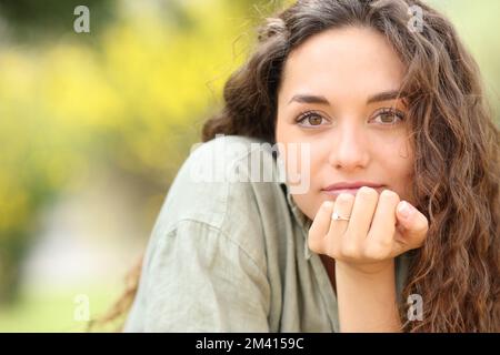 Porträt einer Frau, die dich mit einem Verlobungsring in einem Park ansieht Stockfoto