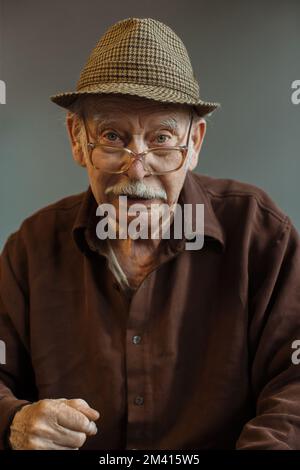 Die alte Generation. Porträt eines Seniorenmannes mit Brille und Hut auf grauem Hintergrund. Stockfoto