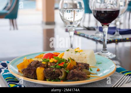 Shish Kebab a-la-Carte-Mahlzeit mit Gemüse und weißem Reis auf einem Teller am Tisch Stockfoto