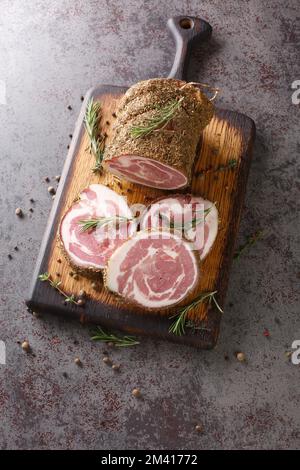 Pancetta ist eine salzgepökelte Schweinefleisch-Bauchfleischrolle auf dem Holzbrett auf dem Tisch. Vertikale Draufsicht von oben Stockfoto