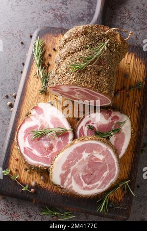 Nahaufnahme eines Holzstücks mit Scheiben italienischer Pancetta-Nahaufnahme. Vertikale Draufsicht von oben Stockfoto
