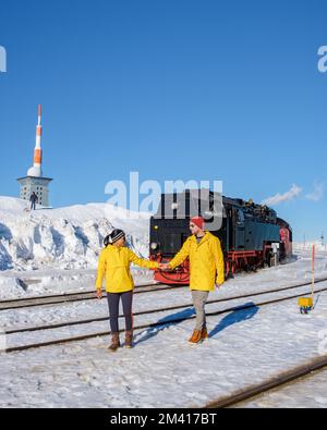 Ein paar Männer und Frauen, die im Winter die Dampfeisenbahn im Schnee im Harz-Nationalpark Deutschland beobachten, Stockfoto