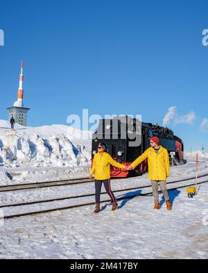 Ein paar Männer und Frauen beobachten die Dampfeisenbahn im Winter im Schnee im Harz-Nationalpark Deutschland, die Dampfeisenbahn Brocken Bahn auf dem Weg durch die Winterlandschaft Stockfoto