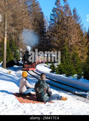 Ein paar Männer und Frauen, die im Winter die Dampfeisenbahn im Schnee im Harz-Nationalpark Deutschland beobachten, Stockfoto