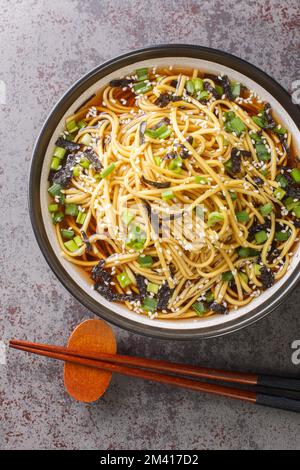 Gekochte Soba-Nudeln werden mit einer Sauce aus Perillaöl, Sojasoße, gerösteten Sesamsamen, Seetang und grünen Zwiebeln in der Schüssel auf t zubereitet Stockfoto
