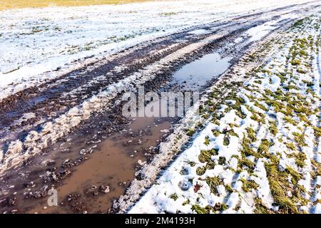 Kleine Pfütze auf der Straße, Reflexion im Wasser nahe der Wiese. Schnee und Winter Stockfoto
